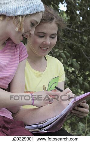 Stock Image - Girls doing homework together in park. Fotosearch