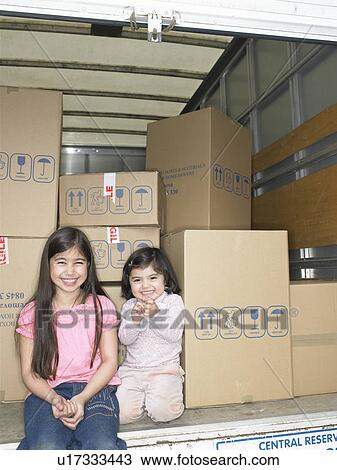 Stock Image - Girls sitting in moving van. Fotosearch