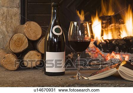 Stock Image - Glass of wine and book by fireplace. Fotosearch