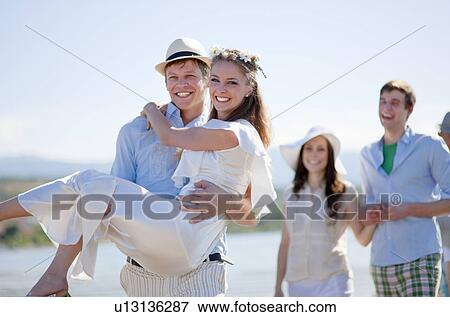 Stock Photo - Groom carrying bride outdoors. Fotosearch