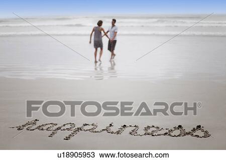 Stock Image - ‘Happiness’ in sand with couple on beach. Fotosearch