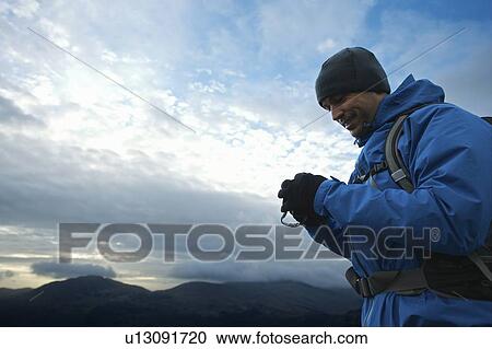 Stock Image - Hiker using digital camera on hillside. Fotosearch