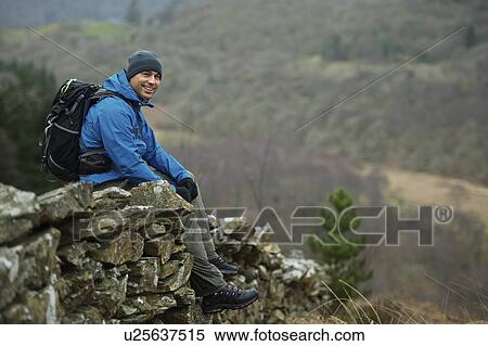 Stock Photography - Hiking man sitting on stone wall. Fotosearch