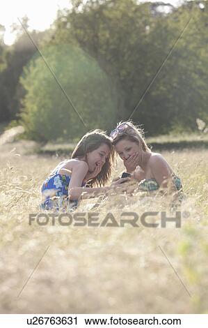 Laughing girls using cell phone in field View Large Photo Image Stock Image - Laughing girls using cell phone in field. Fotosearch