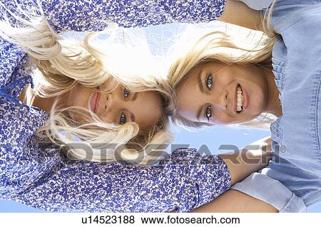 Stock Photo - Low angle view of sisters hugging. Fotosearch