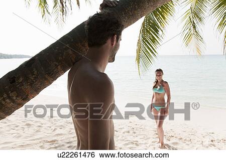 Stock Photograph - Man admiring woman on tropical beach. Fotosearch