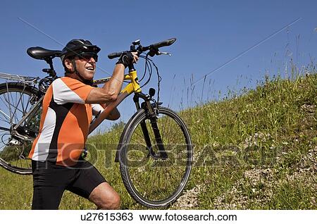 Man carrying bicycle on grassy hillside View Large Photo Image Stock Image - Man carrying bicycle on grassy hillside. Fotosearch