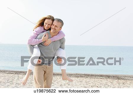 Stock Image - Man carrying girlfriend on beach. Fotosearch