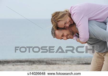 Stock Photo - Man carrying girlfriend on beach. Fotosearch