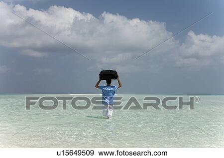 Stock Photo - Man carrying luggage into water at beach. Fotosearch