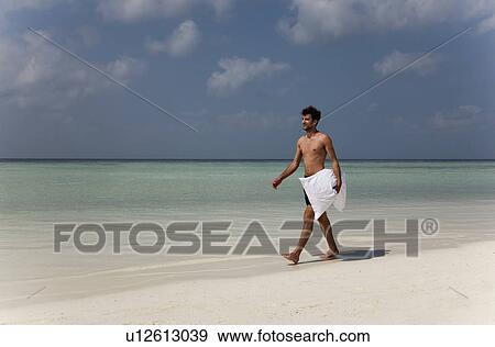 Stock Photo - Man carrying pillow on tropical beach. Fotosearch