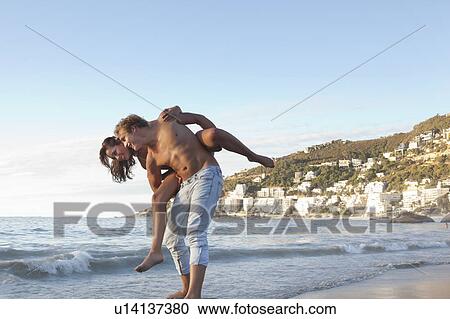 Man carrying woman piggyback on beach View Large Photo Image Stock Image - Man carrying woman piggyback on beach. Fotosearch