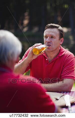 Stock Image - Man drinking beer at picnic table. Fotosearch
