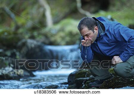 Stock Photograph - Man drinking water from stream. Fotosearch