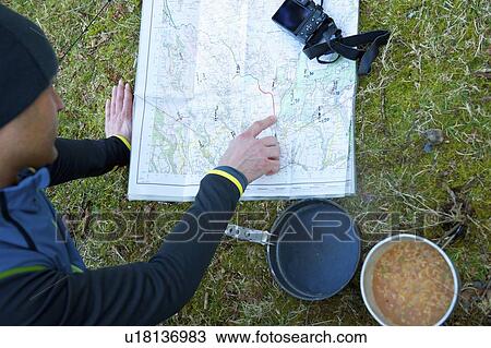 Stock Image - Man examining trail map while camping. Fotosearch