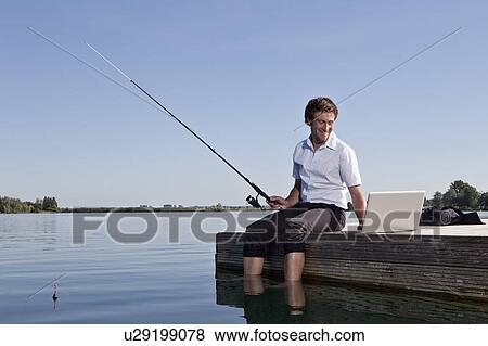 Man fishing and using laptop on dock View Large Photo Image Stock Photo - Man fishing and using laptop on dock. Fotosearch