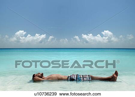 Man floating in water at tropical beach View Large Photo Image Stock Photo - Man floating in water at tropical beach. Fotosearch