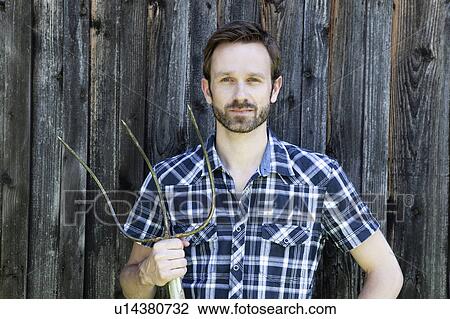 Stock Image - Man holding rake outdoors. Fotosearch