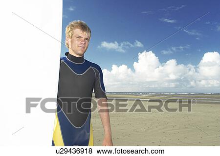 Stock Photo - Man holding surfboard on beach. Fotosearch