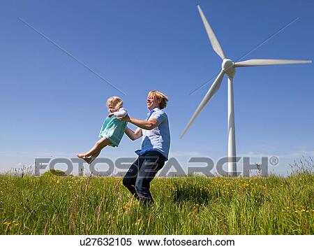 Stock Photography - Man in daughter in field by wind turbine. Fotosearch