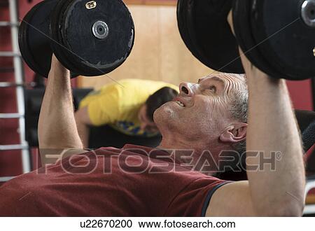 Stock Image - Man lifting weights at gym. Fotosearch