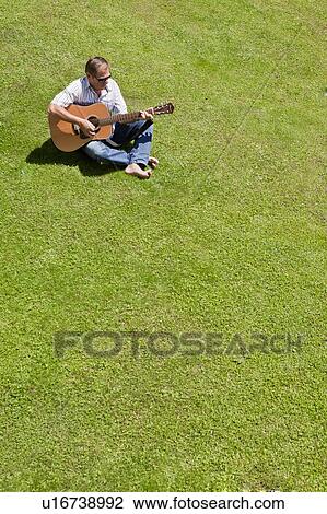 Stock Image - Man playing guitar in grass. Fotosearch
