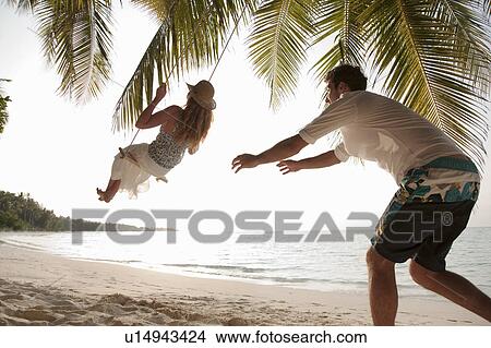 Picture - Man pushing swinging woman at beach. Fotosearch