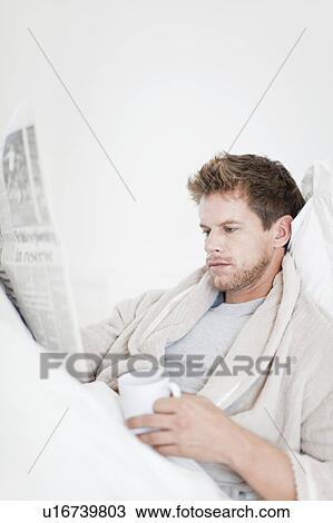 Stock Image - Man reading newspaper in bed. Fotosearch