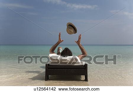 Stock Image - Man relaxing on daybed at tropical beach. Fotosearch