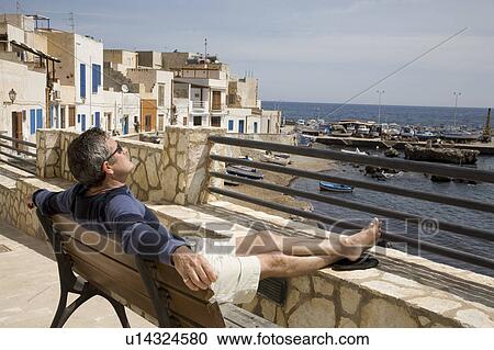 Stock Image - Man relaxing on village street. Fotosearch