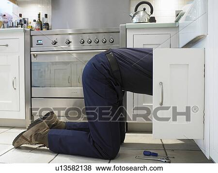 Stock Photo - Man repairing plumbing under sink. Fotosearch