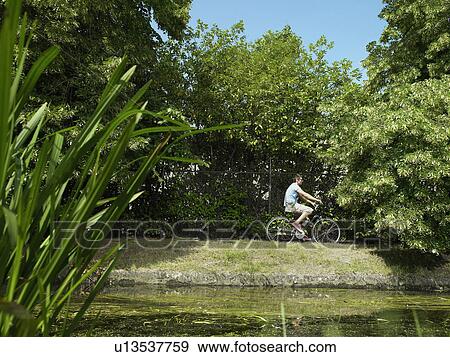 Man riding bicycle on riverbank View Large Photo Image Stock Photo - Man riding bicycle on riverbank. Fotosearch