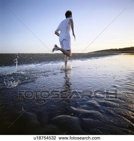 Stock Image - Man running in water on beach. Fotosearch