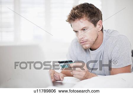 Stock Photograph - Man shopping online in bed. Fotosearch