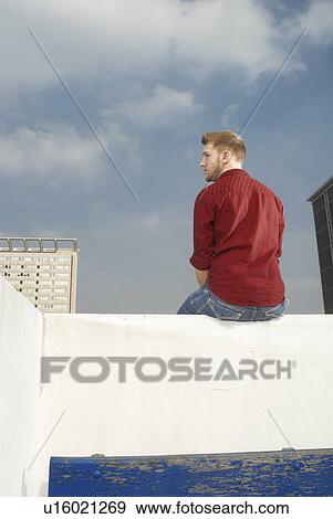 Stock Photo - Man sitting on rooftop wall. Fotosearch