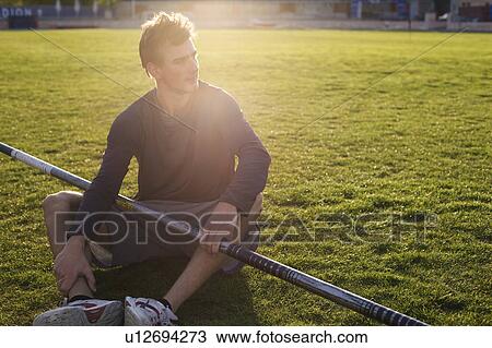 Stock Image - Man sitting with pole on grass. Fotosearch