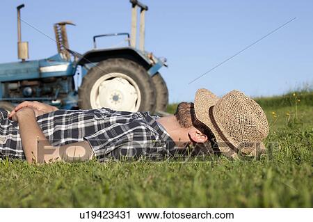 Stock Image - Man sleeping with hat over eyes in field. Fotosearch