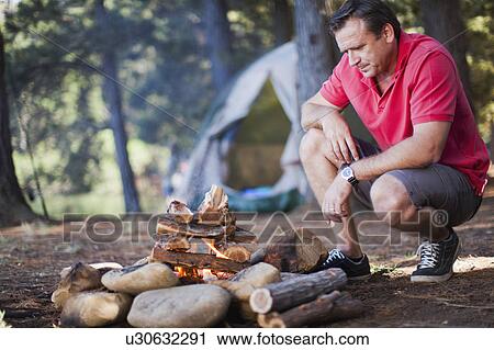 Man starting a fire at campsite View Large Photo Image Stock Image - Man starting a fire at campsite. Fotosearch