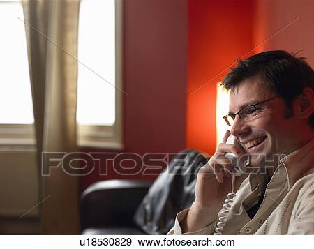 Stock Photo - Man talking on phone in living room. Fotosearch