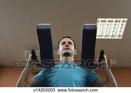 Stock Image - Man using exercise machine in gym. Fotosearch