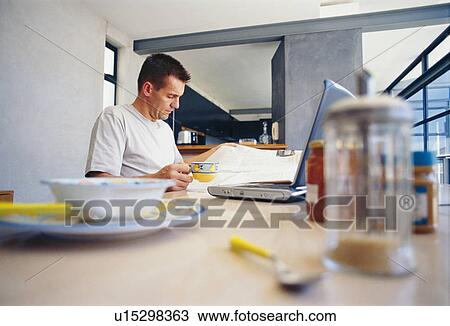 Stock Image - Man using laptop at breakfast. Fotosearch