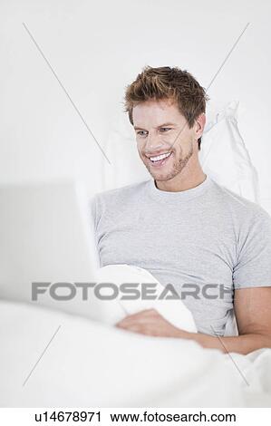 Man using laptop in bed View Large Photo Image Stock Image - Man using laptop in bed. Fotosearch