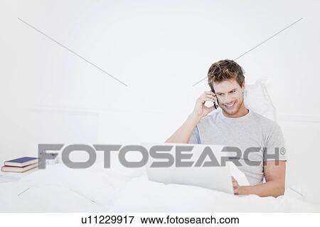 Stock Photo - Man using laptop in bed. Fotosearch