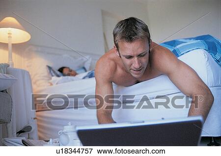 Stock Photo - Man using laptop in bedroom. Fotosearch