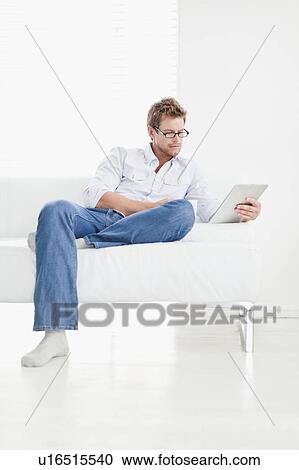 Man using tablet on couch View Large Photo Image Stock Image - Man using tablet on couch. Fotosearch