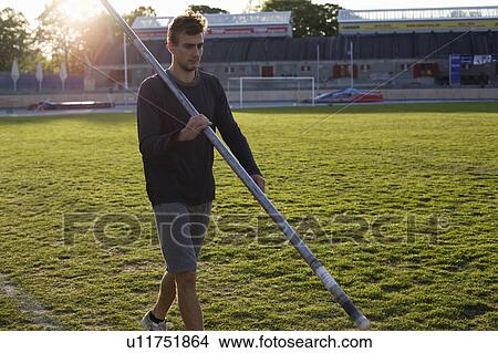 Picture - Man walking with pole on stadium grass. Fotosearch