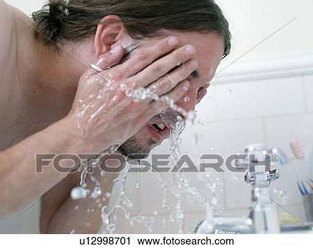 Stock Image - Man washing his face in bathroom. Fotosearch