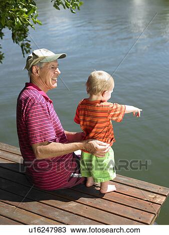 Stock Image - Man with grandson on jetty over lake. Fotosearch