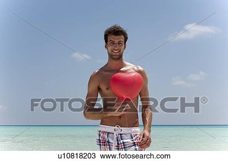 Stock Image - Man with heart shaped balloon on beach. Fotosearch