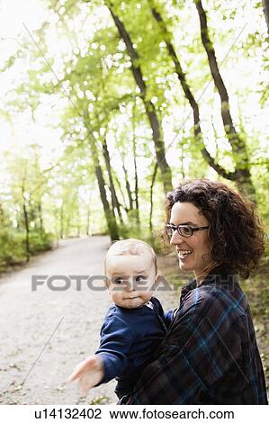 Stock Image - Mother carrying baby in park. Fotosearch